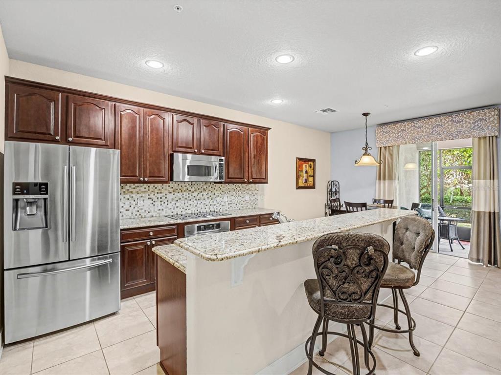 A kitchen features dark wood cabinets, granite countertops, stainless steel appliances, and a breakfast bar — 1405 LISBON COURT, DAVENPORT, FL