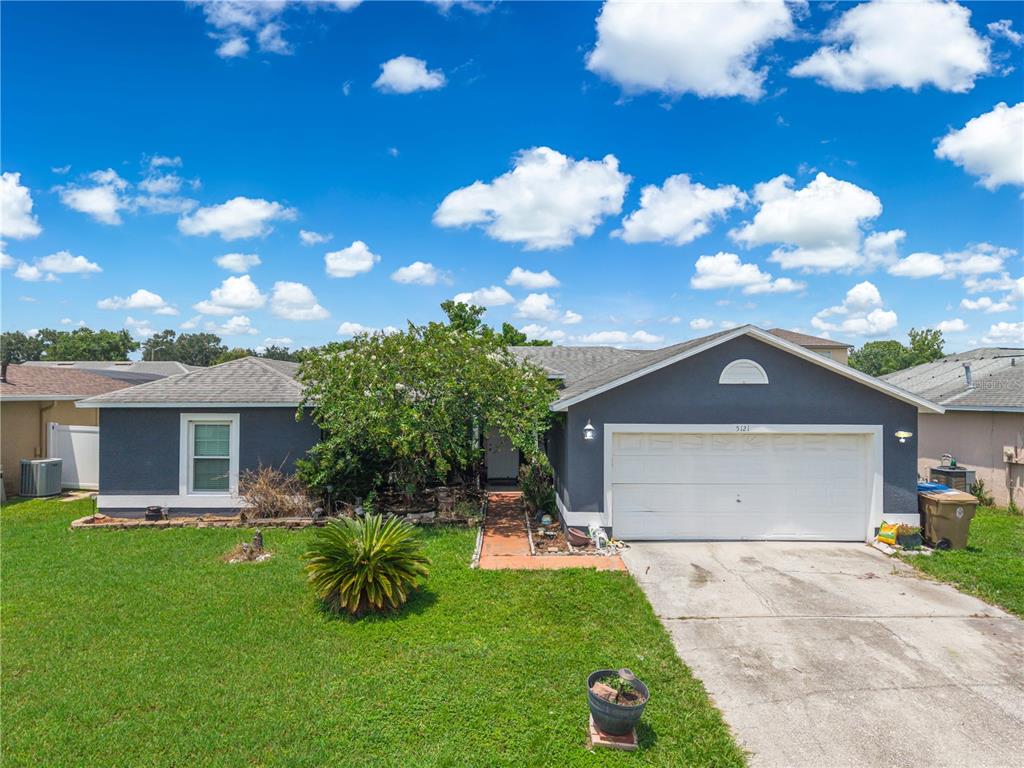 A single-story house with a dark gray exterior, a two-car garage, and a front lawn — 5121 HEATHERSTONE COURT, KISSIMMEE, FL