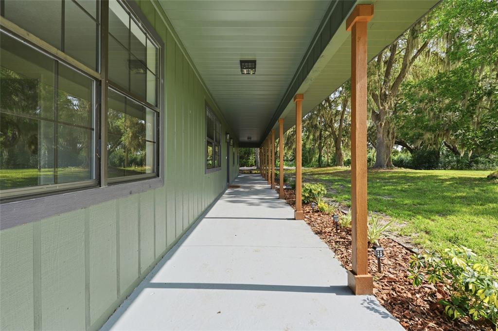 A long, covered porch with wooden support posts runs along the side of a green house — 4351 NE 210TH AVENUE, WILLISTON, FL