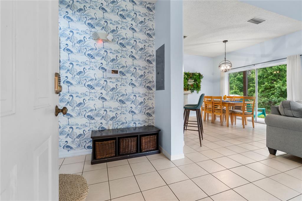An entryway features flamingo-patterned wallpaper, a dark storage bench, and tile flooring — 2733 SUN KEY PLACE, KISSIMMEE, FL
