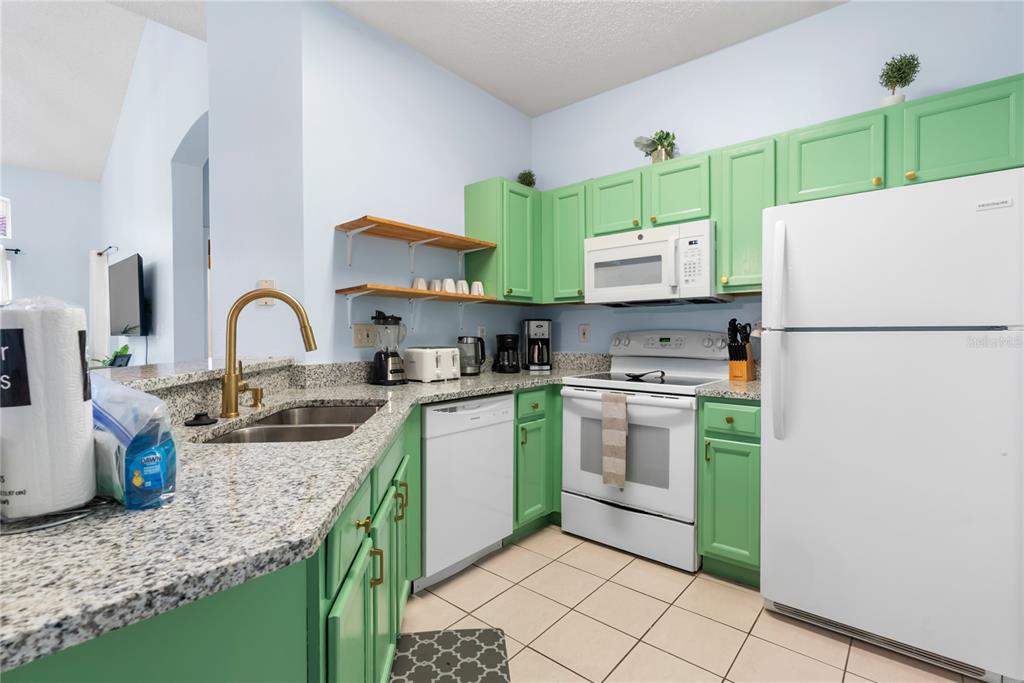 A kitchen features green cabinets, granite countertops, a white refrigerator, and a white dishwasher — 2733 SUN KEY PLACE, KISSIMMEE, FL