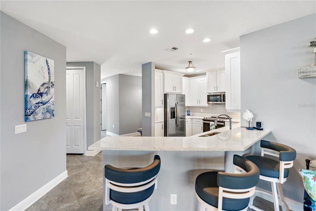 A kitchen with white cabinets, stainless steel appliances, and a breakfast bar with three stools — 7840 34TH AVENUE W UNIT 103, BRADENTON, FL