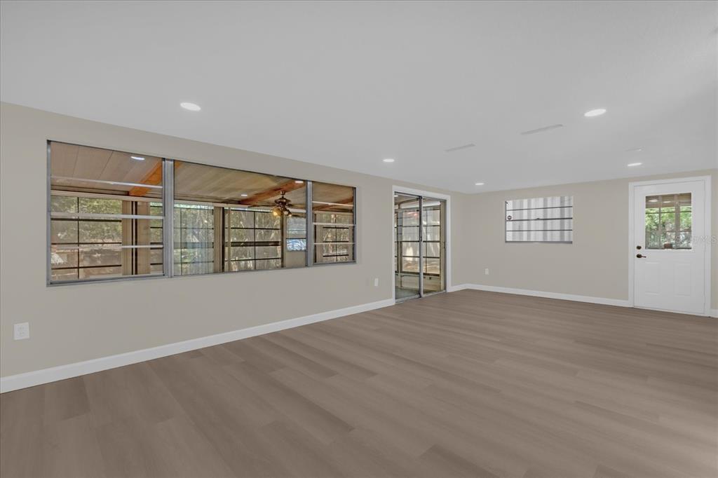 An empty room with light-colored walls, wood-look flooring, large windows, and a white door — 1610 GLENWOOD ROAD, DELAND, FL