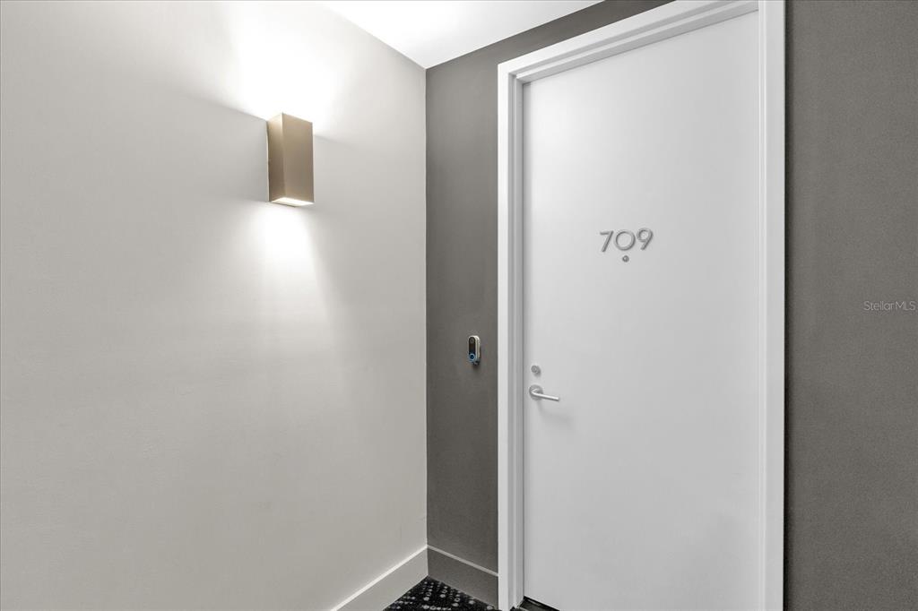 A white door labeled 709 is set against a gray wall next to a wall sconce — 260 S OSCEOLA AVENUE UNIT 709, ORLANDO, FL