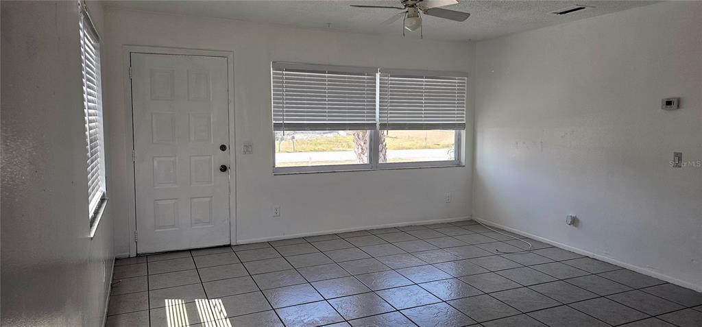 An empty room features white walls, tiled flooring, a ceiling fan, and a front door — 12048 HENLEY AVENUE UNIT A & B, PORT CHARLOTTE, FL