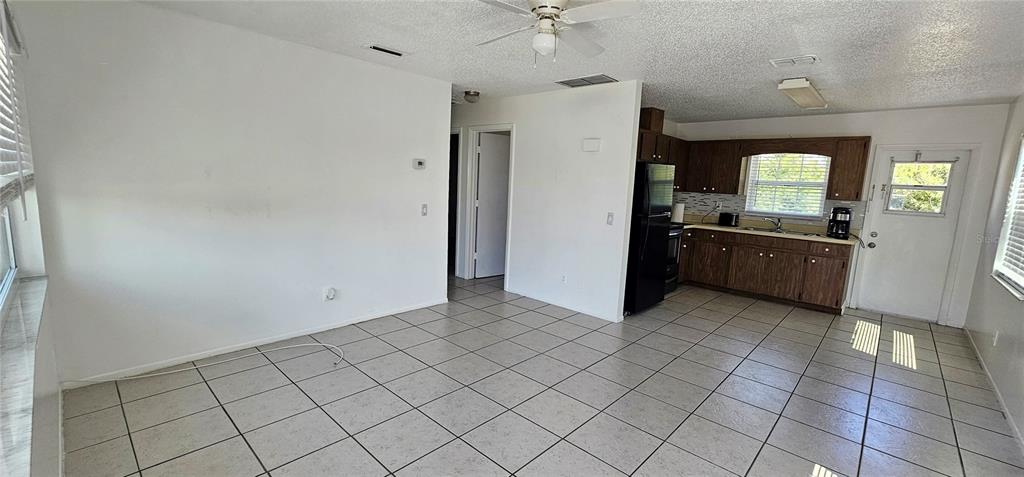 An open-concept room features white walls, tiled floors, a ceiling fan, and a wood-cabinet kitchen — 12048 HENLEY AVENUE UNIT A & B, PORT CHARLOTTE, FL