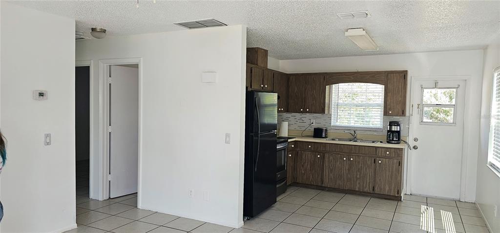 A kitchen with wood cabinets, a black refrigerator, and tile flooring opens to a hallway — 12048 HENLEY AVENUE UNIT A & B, PORT CHARLOTTE, FL