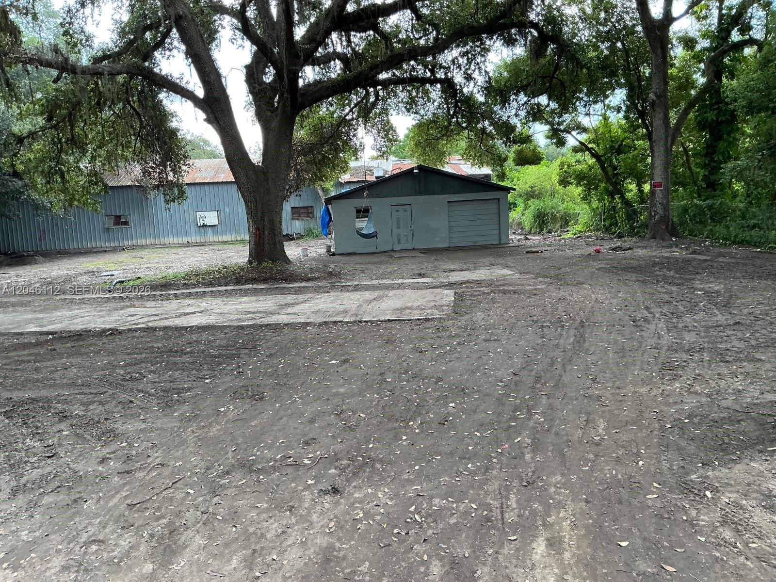 A dirt lot features a small gray garage and a large metal building under trees — 1035 David Street Lakeland, FL 338012, FL