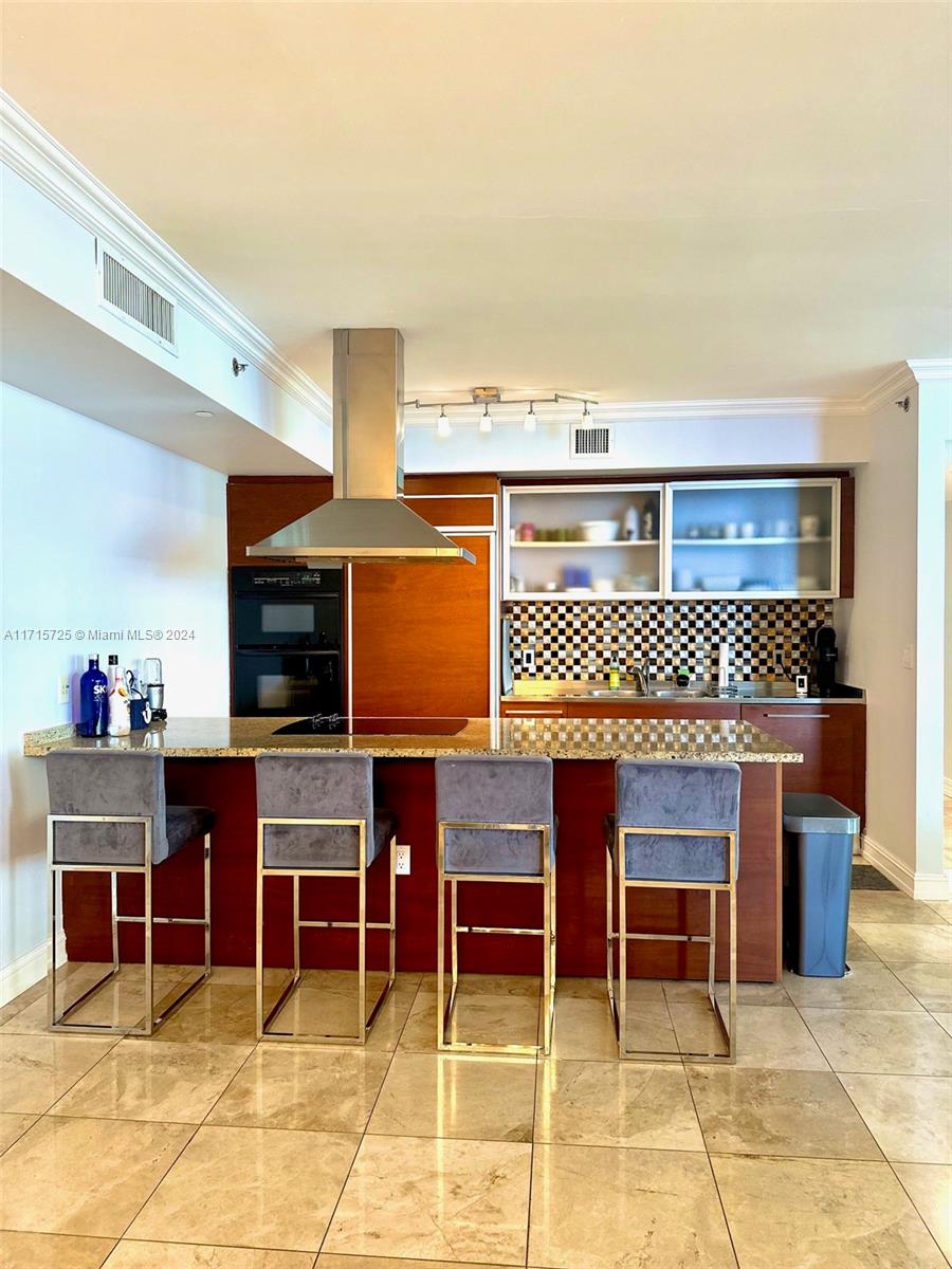 A kitchen features a granite island with four bar stools, wood cabinetry, and stainless appliances — 1850 S Ocean Dr # 3310, Hallandale Beach FL 33009, HALLANDALE BEACH, FL