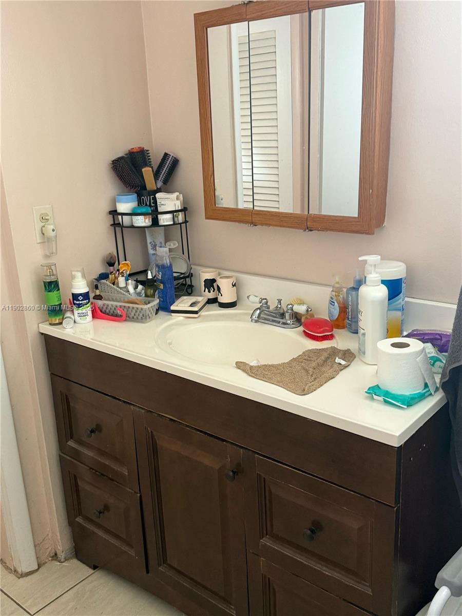 A bathroom vanity features a white countertop, dark wood cabinets, and a tri-fold medicine cabinet — 18555 NE 14th Ave # 715, Miami FL 33179, MIAMI, FL