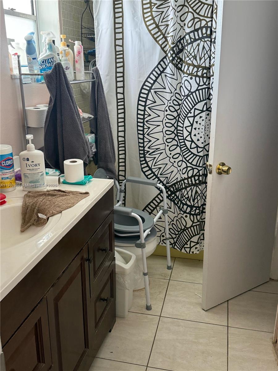 A bathroom features a vanity, a toilet with a safety frame, and a patterned shower curtain — 18555 NE 14th Ave # 715, Miami FL 33179, MIAMI, FL