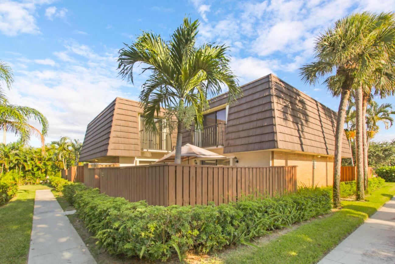A two-story building with a brown mansard roof, wooden privacy fence, and surrounding palm trees — 1909 19th Court # 33a, Jupiter FL 33477, JUPITER, FL