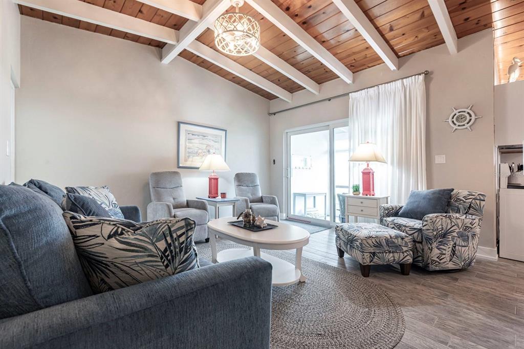 A living room features a vaulted wood-beam ceiling, gray furniture, and a circular area rug — 6006 MIDNIGHT PASS ROAD UNIT 22, SARASOTA, FL