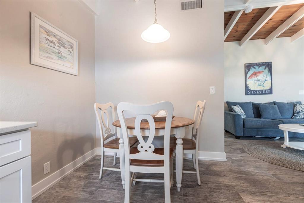 A dining area with a round wooden table and white chairs sits near a living room — 6006 MIDNIGHT PASS ROAD UNIT 22, SARASOTA, FL