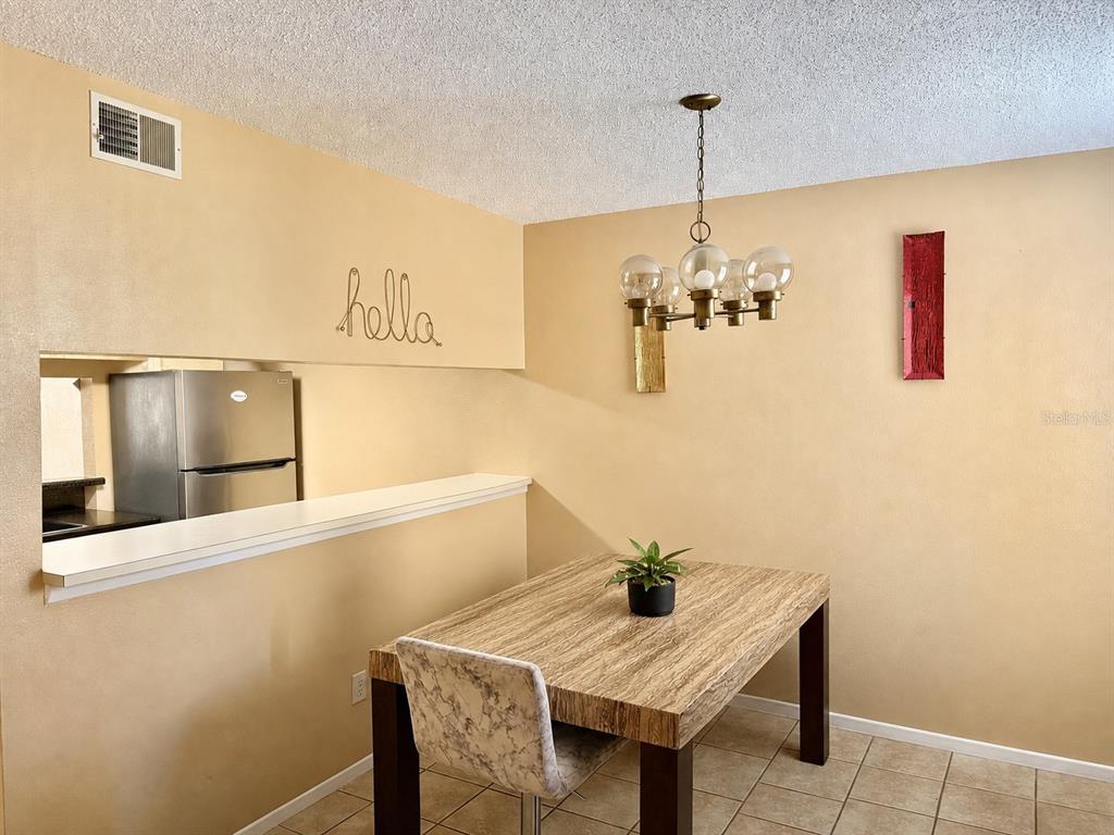 A dining area features a wood-grain table, a modern chandelier, and a kitchen pass-through window — 7011 WATERSIDE DR, TAMPA, FL