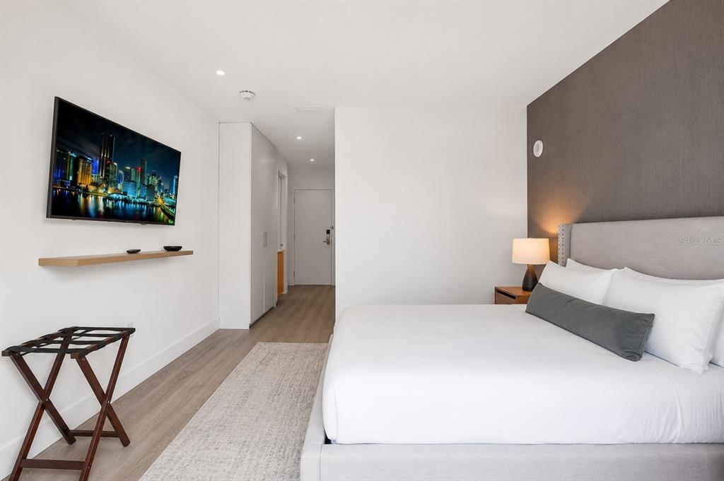 A modern bedroom features a king bed, wall-mounted television, and light wood-look flooring — 229 SW 9TH STREET UNIT 406, MIAMI, FL