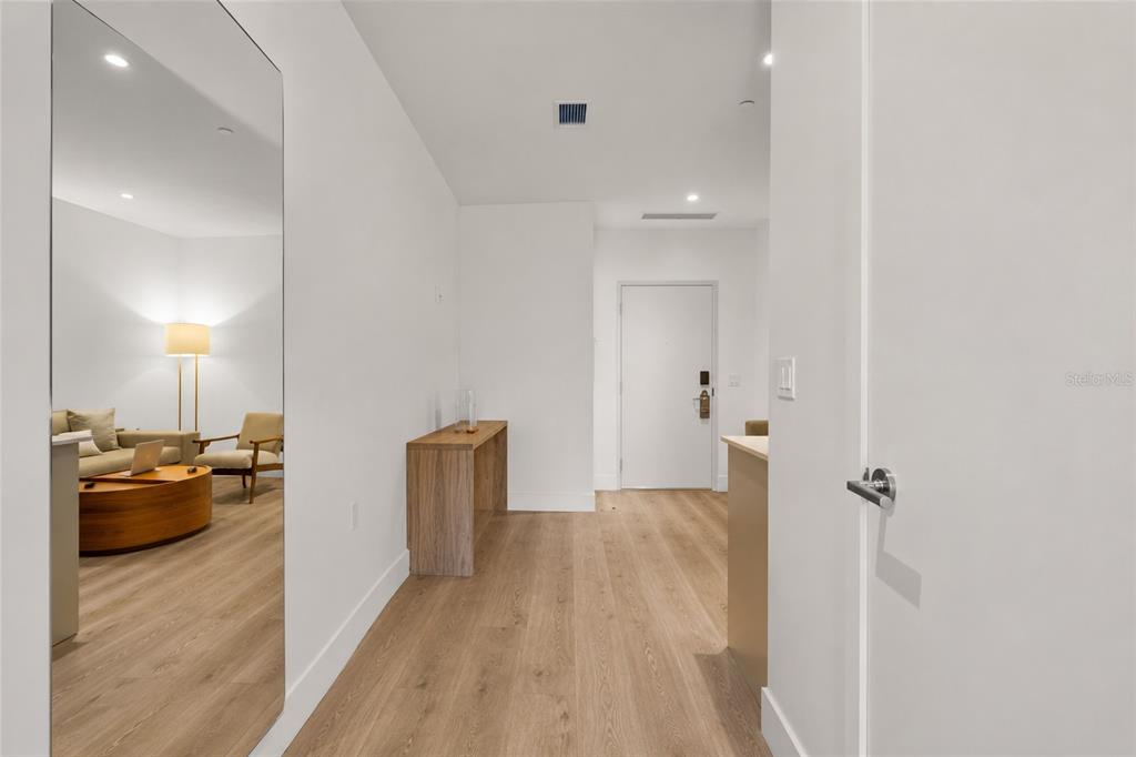 A hallway with light wood flooring leads to a white door and a large mirror — 229 SW 9TH STREET UNIT 406, MIAMI, FL