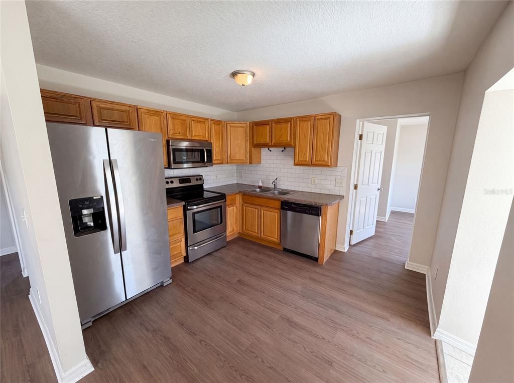 A kitchen features stainless steel appliances, wood cabinets, a subway tile backsplash, and wood-look flooring — 1604 PARK AVENUE, MELBOURNE, FL