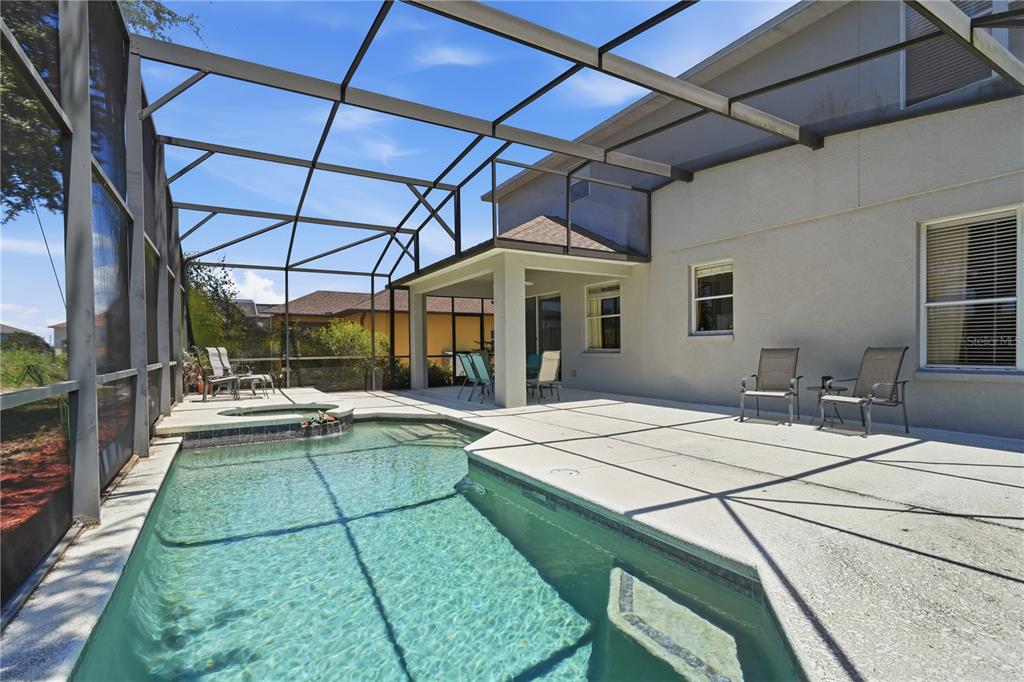 A swimming pool and spa are enclosed within a screened lanai behind a house — 600 WILDFLOWER ROAD, DAVENPORT, FL