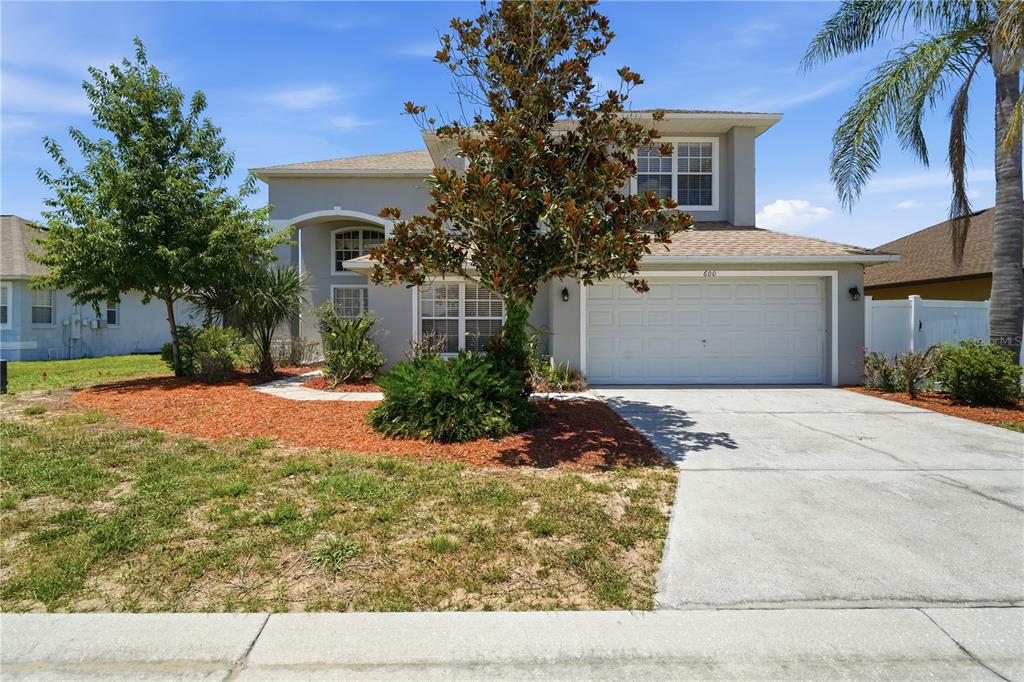A two-story suburban house with a white garage, gray exterior, and a front yard — 600 WILDFLOWER ROAD, DAVENPORT, FL