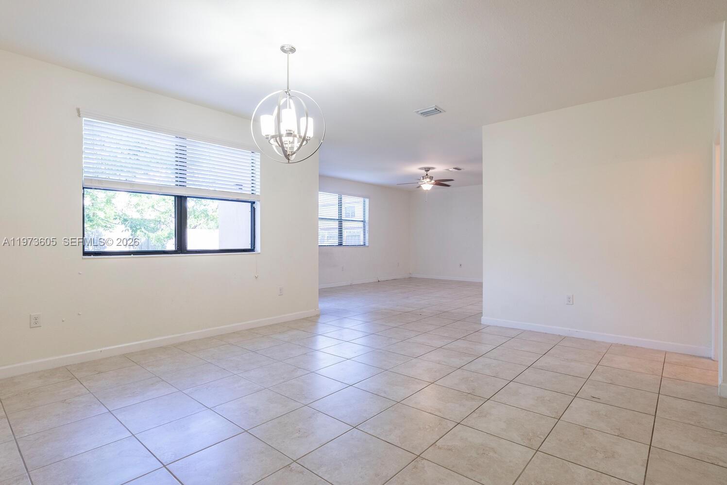 An open dining area features light tile flooring, a modern chandelier, and large windows — 516 SE 35th Ter, Homestead FL 33033, HOMESTEAD, FL