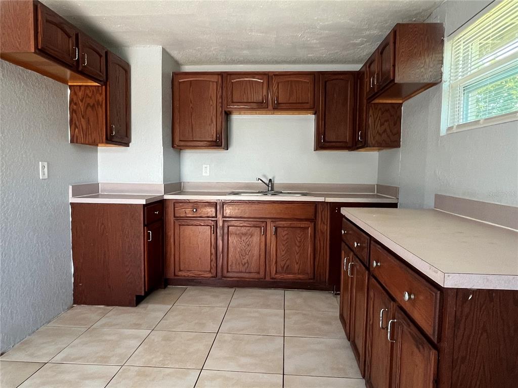 A kitchen features dark wood cabinets, beige countertops, and light-colored tile flooring — 1142 MARTIN STREET, HAINES CITY, FL
