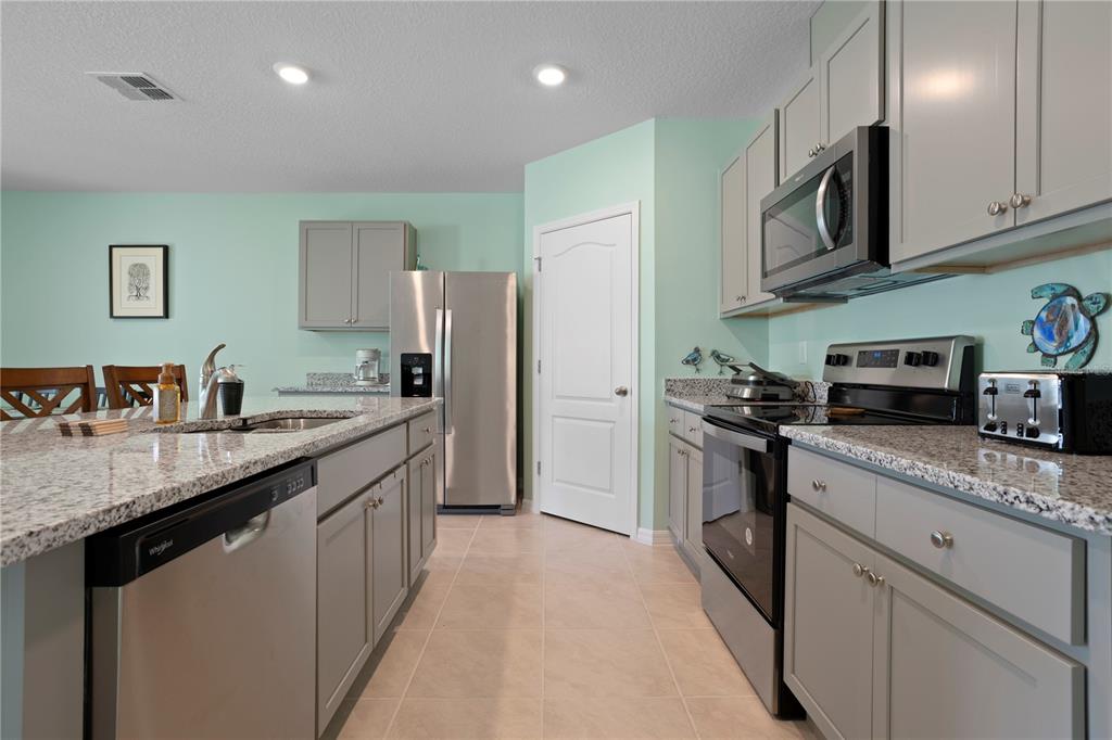A kitchen features gray cabinets, granite countertops, stainless steel appliances, and light green walls — 2648 NEVERLAND DRIVE, NEW SMYRNA BEACH, FL