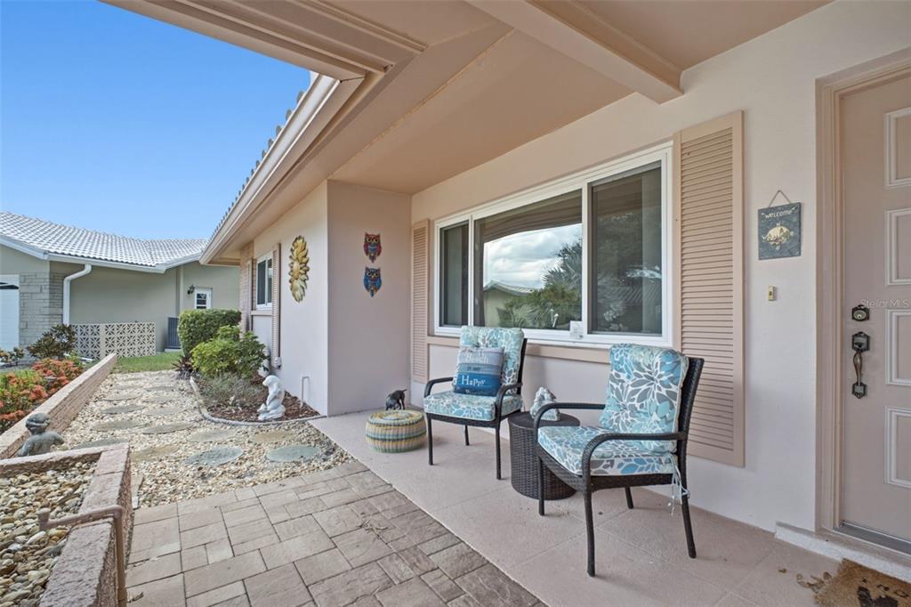 A covered front porch features two patterned chairs, a small table, and a stone walkway — 1520 KENMORE COURT, PALM HARBOR, FL