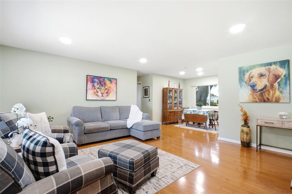 A living room with hardwood floors, a gray sectional, and plaid armchairs leads to a dining area — 1520 KENMORE COURT, PALM HARBOR, FL
