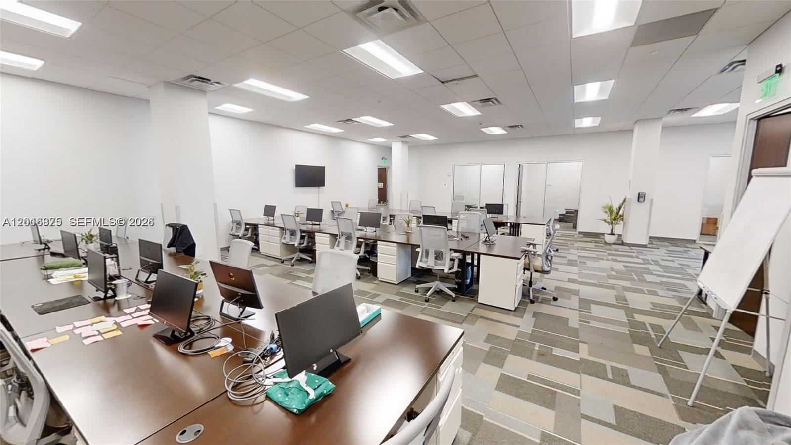 An open-plan office space features rows of desks, computer monitors, and patterned carpet flooring — 1501 Biscayne # 501, Miami FL 33132, MIAMI, FL