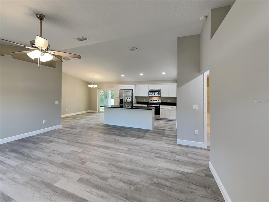 An open-concept living area features light wood-look flooring, a kitchen island, and white cabinetry — 2082 W SWANSON DRIVE, CITRUS SPRINGS, FL