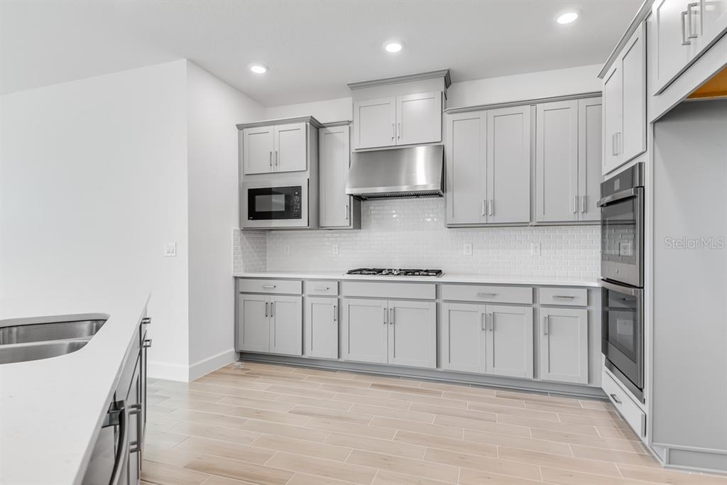 A modern kitchen features gray cabinets, a white quartz island, and three black bar stools — 668 JUNONIA BOULEVARD, NEW SMYRNA BEACH, FL
