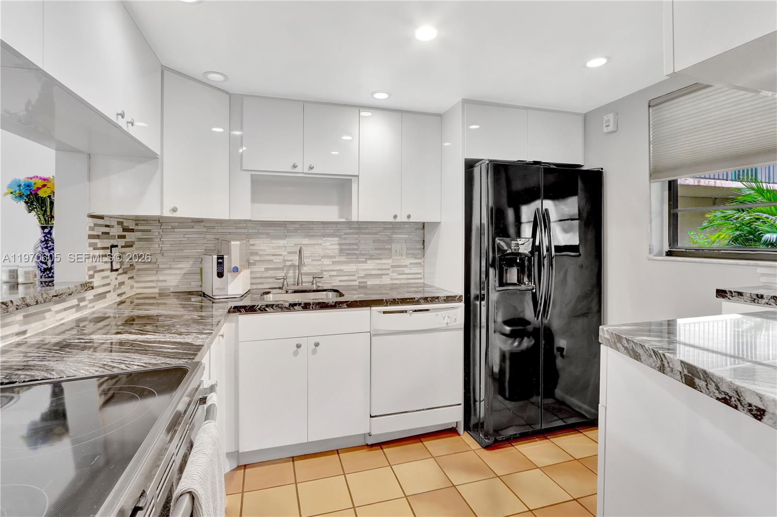 A kitchen features white cabinets, a black refrigerator, dark stone countertops, and tan floor tiles — 10525 SW 112th Ave # 117, Miami FL 33176, MIAMI, FL