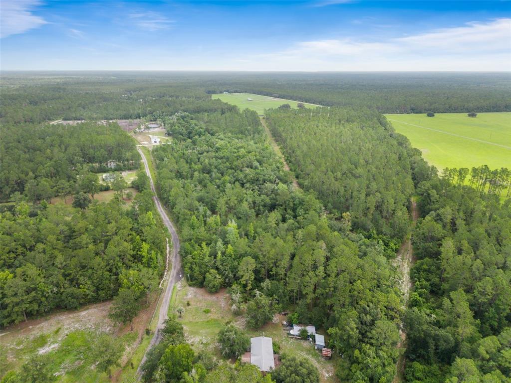An aerial view shows a house surrounded by dense forest, a dirt road, and pastures — TBD RETREAT ROAD, KEYSTONE HEIGHTS, FL