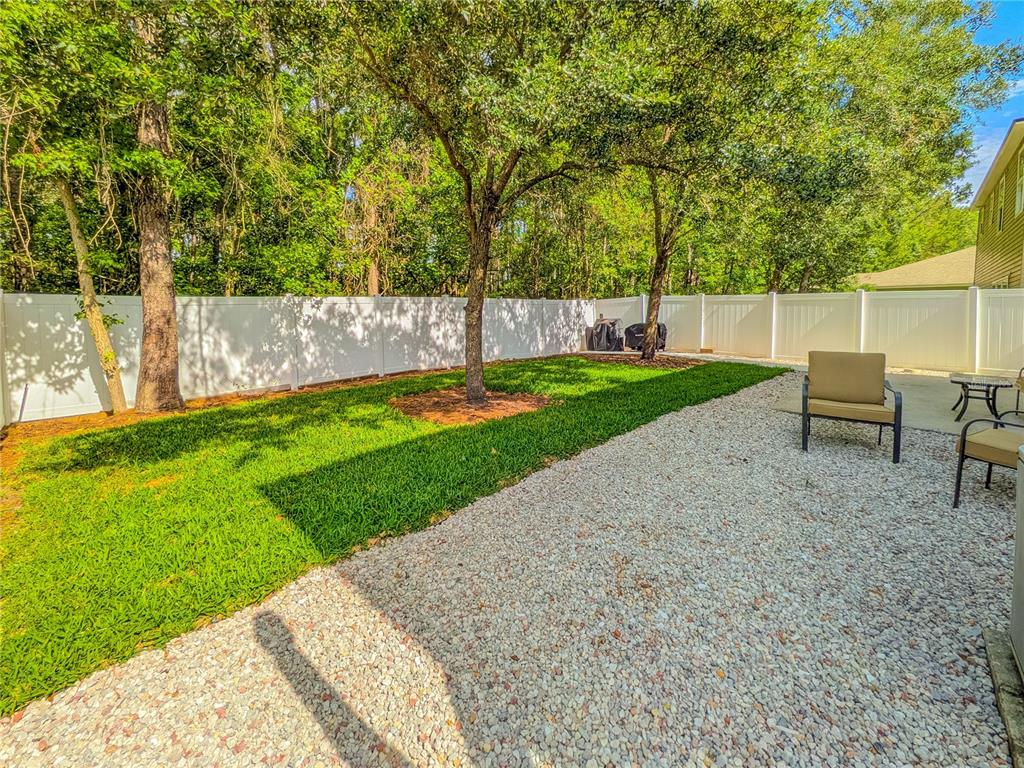 A backyard features a gravel patio, a patch of green grass, and a white privacy fence — 12101 ALEXANDRA DRIVE, JACKSONVILLE, FL