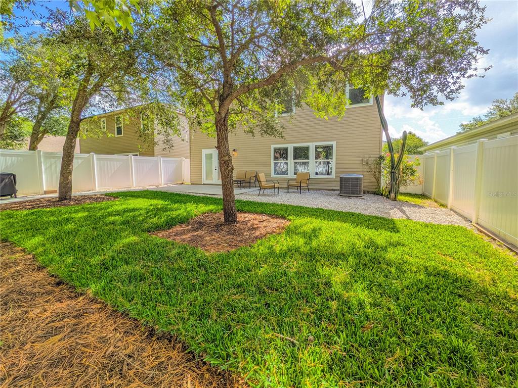 A backyard features a grassy lawn, a gravel patio with chairs, and a white fence — 12101 ALEXANDRA DRIVE, JACKSONVILLE, FL