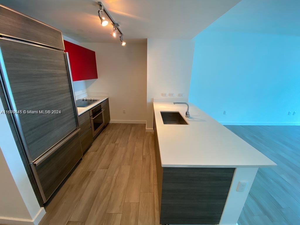 A modern kitchen features wood-grain cabinetry, a white countertop island, and stainless steel appliances — 1100 S Miami Ave # 2602, Miami FL 33130, MIAMI, FL