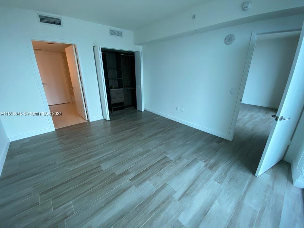 An empty bedroom features light wood-look tile flooring, white walls, and a walk-in closet — 1100 S Miami Ave # 2602, Miami FL 33130, MIAMI, FL