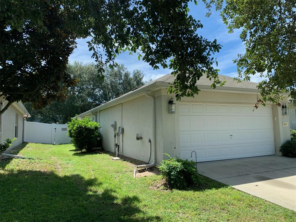 The side view of a house shows a garage door, a white fence, and landscaping — 4311 SW 53RD TERRACE, OCALA, FL