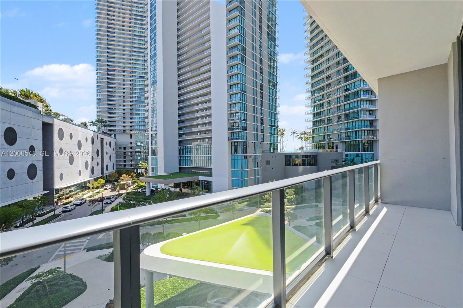 A balcony with a glass railing overlooks a modern urban complex with tall residential towers — 501 NE 31st St # 302, Miami FL 33137, MIAMI, FL
