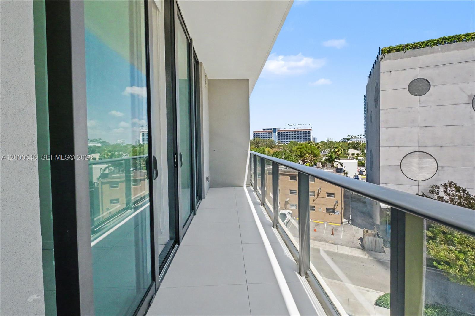 A modern balcony features large glass sliding doors, light tile flooring, and a glass railing — 501 NE 31st St # 302, Miami FL 33137, MIAMI, FL