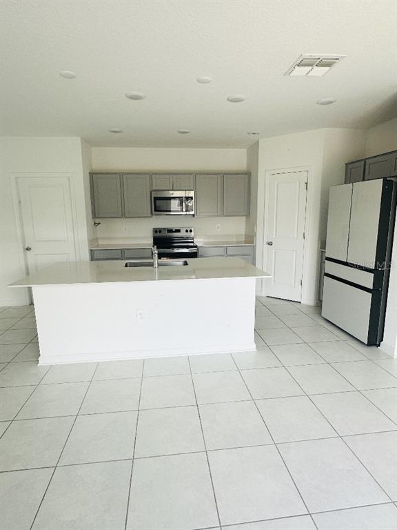 A kitchen features gray cabinets, stainless steel appliances, a white island, and light tile flooring — 2847 BIG SUR ROAD, DAVENPORT, FL