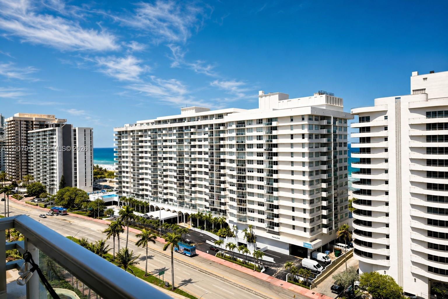 An elevated exterior view of white high-rise residential buildings near a beach and road — 5600 Collins Ave # 15B, Miami Beach FL 33140, MIAMI BEACH, FL