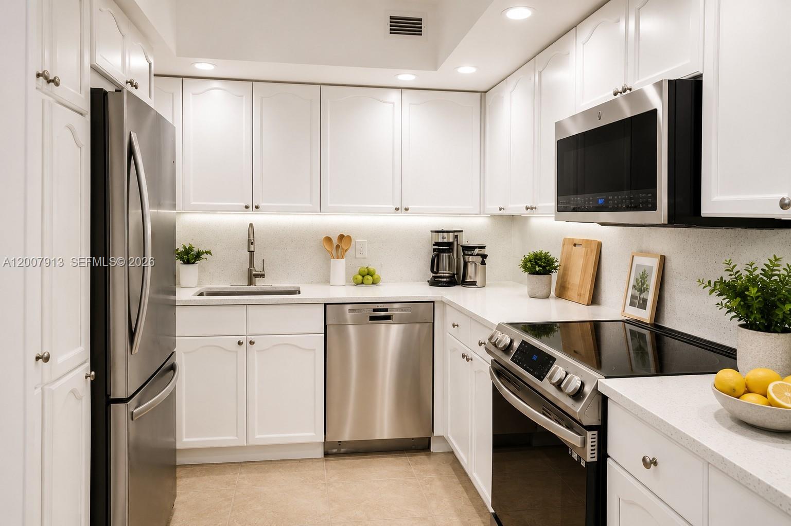 A white kitchen features stainless steel appliances, quartz countertops, and under-cabinet lighting — 5600 Collins Ave # 15B, Miami Beach FL 33140, MIAMI BEACH, FL