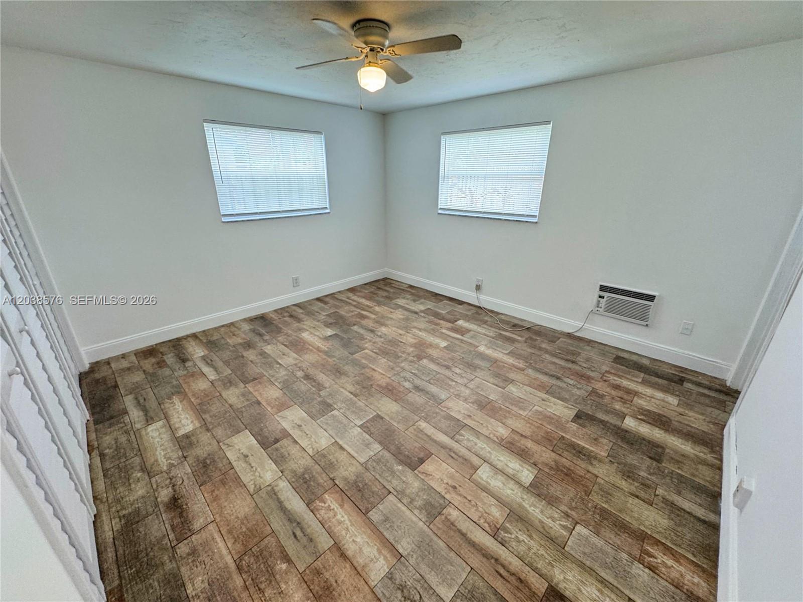 An empty bedroom features white walls, wood-look tile flooring, two windows, and a ceiling fan — 207 SE 4th Ave, Boynton Beach FL 33435, BOYNTON BEACH, FL