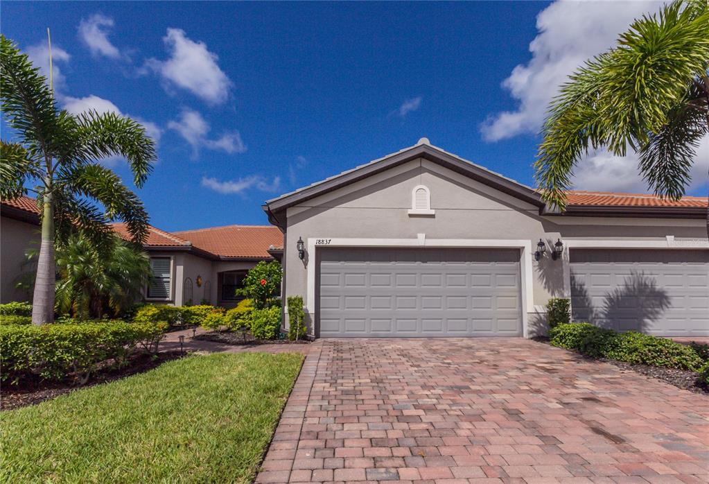 A beige house with a brick paver driveway and a two-car garage under a blue sky — 18837 LANUVIO STREET, VENICE, FL