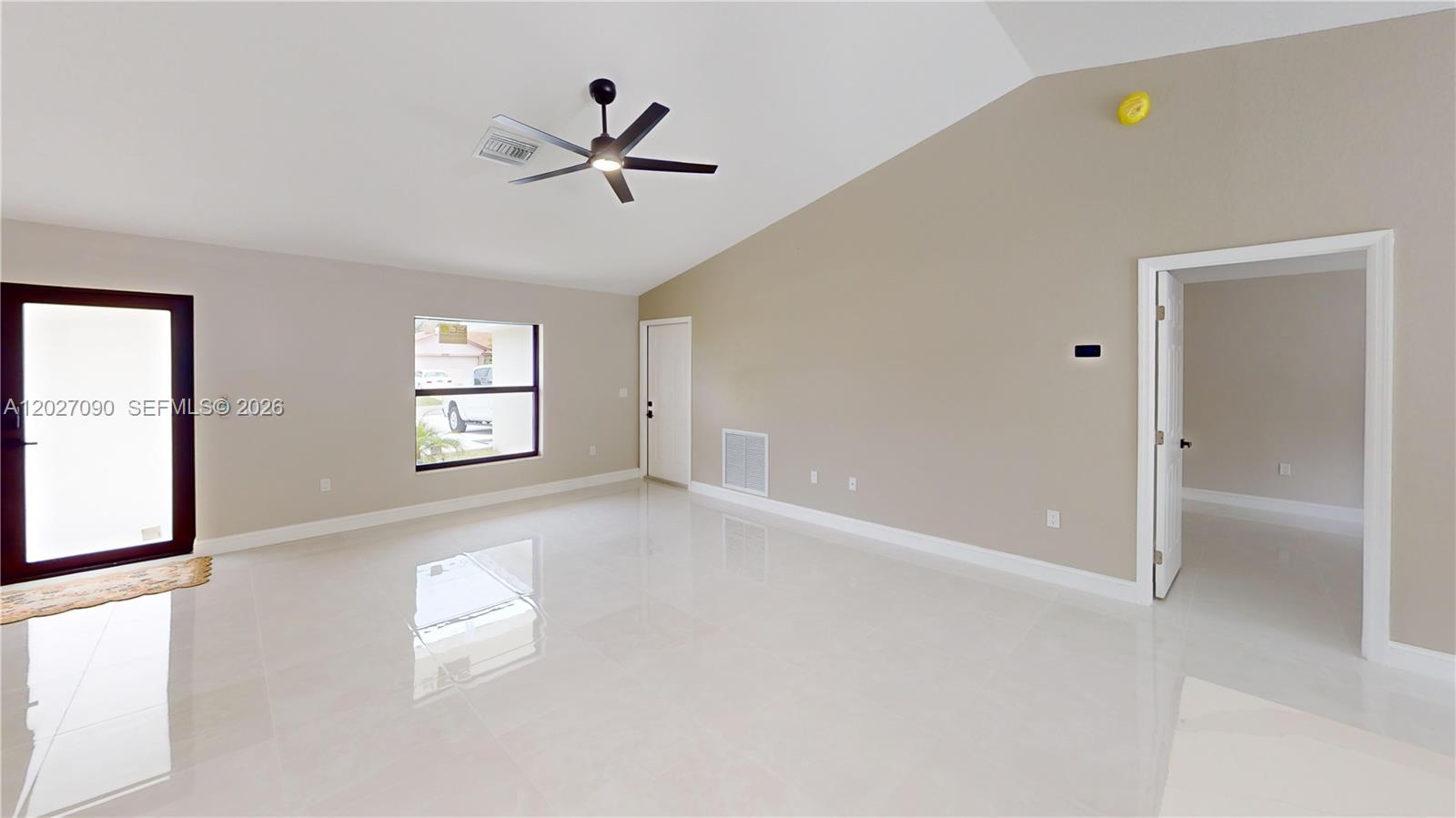 A bright, empty living room features white tile floors, a vaulted ceiling, and a fan — 4726 Trout Ave, Sebring FL 33870, SEBRING, FL