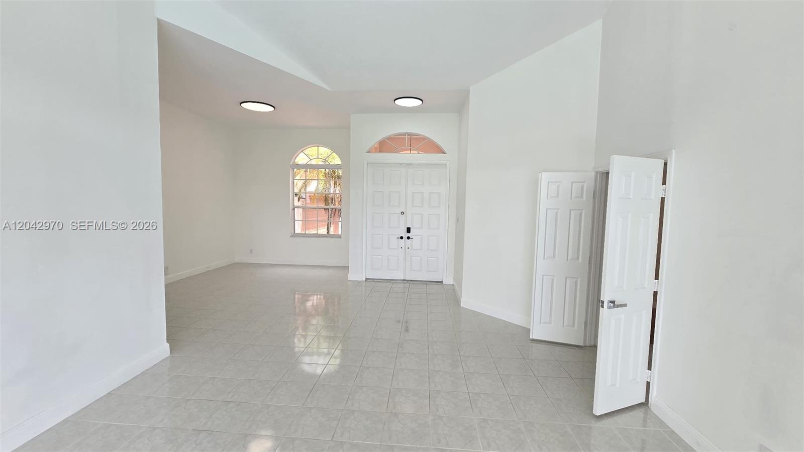 An empty room features white walls, tile flooring, a double front door, and arched windows — 10320 Guatemala St, Cooper City FL 33026, COOPER CITY, FL