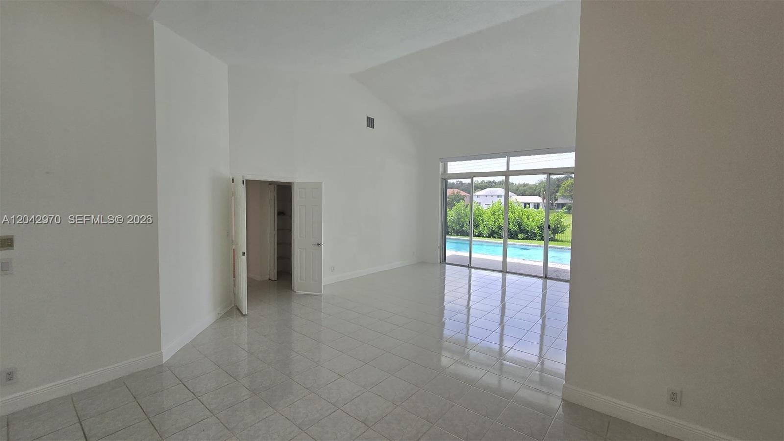 A bright, tiled living room features high vaulted ceilings and sliding doors overlooking a pool — 10320 Guatemala St, Cooper City FL 33026, COOPER CITY, FL