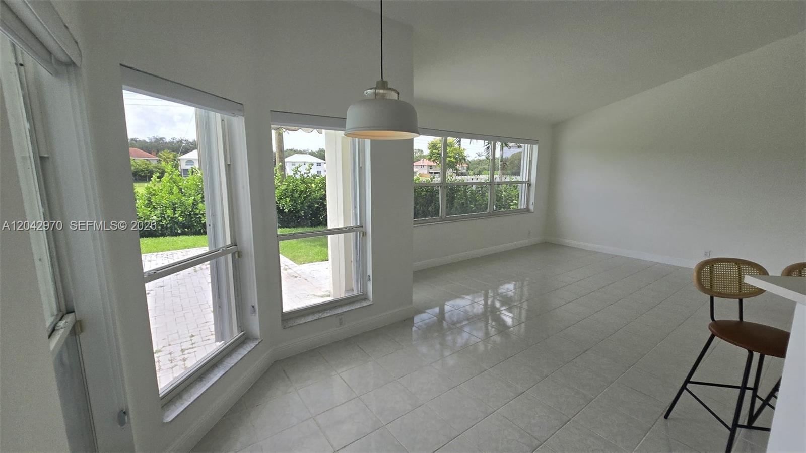 A bright, tiled dining area features large windows, a pendant light, and a bar stool — 10320 Guatemala St, Cooper City FL 33026, COOPER CITY, FL